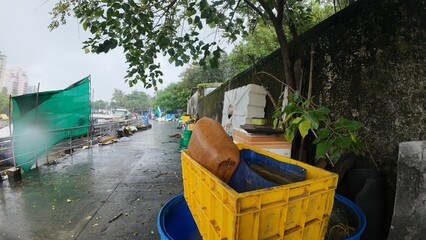 A Close-Up View of Wet, Old Yellow Plastic Crates and Blue Baskets During a Cloudy, Overcast Rainy Day in a Tropical City
