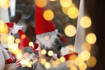 Woman with Christmas gnome near window at home, closeup. Bokeh effect