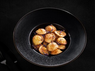 Delicious golden ravioli fills a modern black bowl, creating an inviting contrast. Garnished with delicate herbs, the presentation enhances the warm, cozy atmosphere of an intimate dining setting