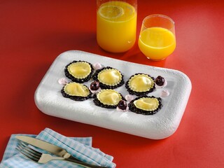 Handcrafted ravioli filled with creamy goodness rests on a white plate atop a bright red table. Refreshing orange drinks complement the meal, creating a joyful dining moment