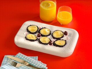 Lively atmosphere showcases artisanal ravioli garnished with cherries on a colorful plate. Two glasses of orange juice complete the delightful meal for a cheerful afternoon