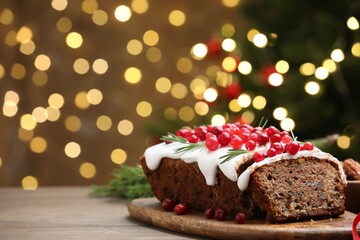 Tasty Christmas cake with icing, cranberries and rosemary on wooden table against background with blurred lights, closeup