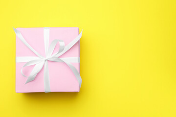 One gift box with ribbon on yellow background, top view. Space for text