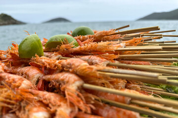 Close-up of grilled shrimp skewers topped with fresh lime halves, photographed against a blurred ocean background 