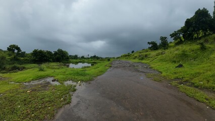Lush Green Western Ghats Landscape: A Dirt Road Winding Through Rain-Soaked Hills and Dense Vegetation Under a Moody, Overcast Sky