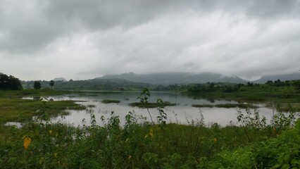 Serene Lake Landscape Surrounded by Greenery and Misty Mountains Under Cloudy Monsoon Sky