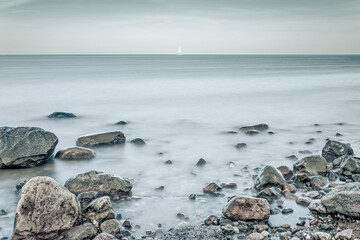 Rocks in the water on the Baltic Sea coast with sailboat on the horizon.