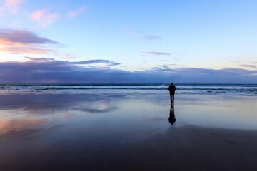 Paisaje de horizonte en el mar en un cielo reflejado en la arena mojada y una presona al flndo de...