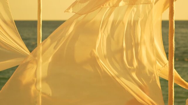 Sheer fabric drapes blowing gently in the wind at golden hour on a serene beach with the ocean in the background