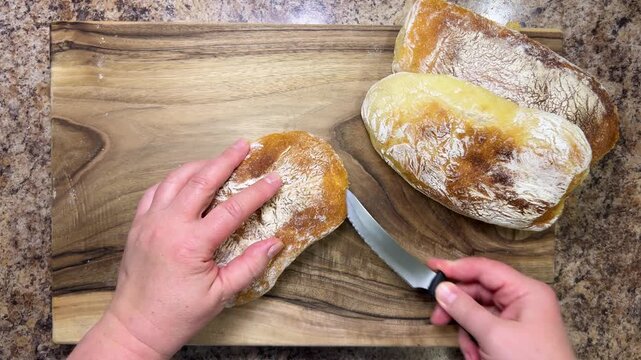 A freshly baked, delicious loaf of homemade ciabatta is cut lengthwise into two halves on a wooden board. Ciabatta on a walnut wooden cutting board.