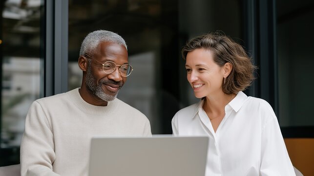 Manager and new employee sitting by a sunlit window during an early feedback session, laptop open between them — warm and authentic visual of leadership, trust, and career growth through open