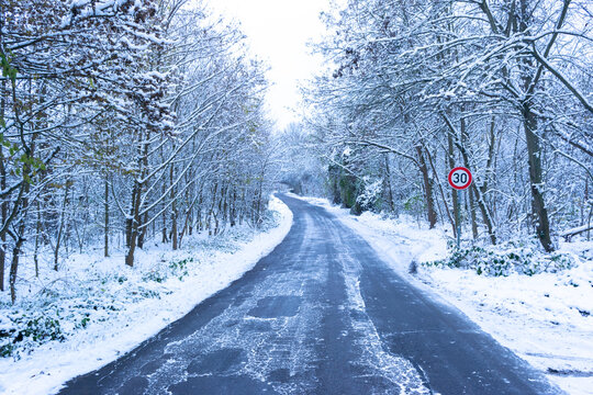 Asphalt road covered with ice among snowy forest. Road sign speed limit "30".