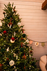 Christmas tree in a wooden house decorated with white, red and green velvet balls with a triangular fabric garland on the wall