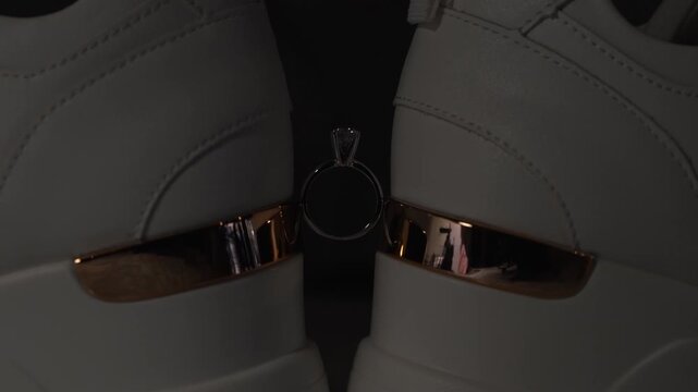 A diamond engagement ring suspended between two white sneakers with rose gold details. This modern concept blends luxury and casual style, perfect for fashion or jewelry advertising.