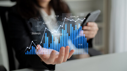 A businesswoman reviews financial data trends using a smartphone and digital graphs, showcasing modern technology in a dynamic office environment. Scalp