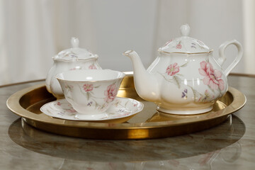 Elegant floral teapot and teacup set on a gold tray for a refined tea setting