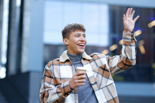 Smiling man in shirt with takeaway cup waving hello on city street - Powered by Adobe