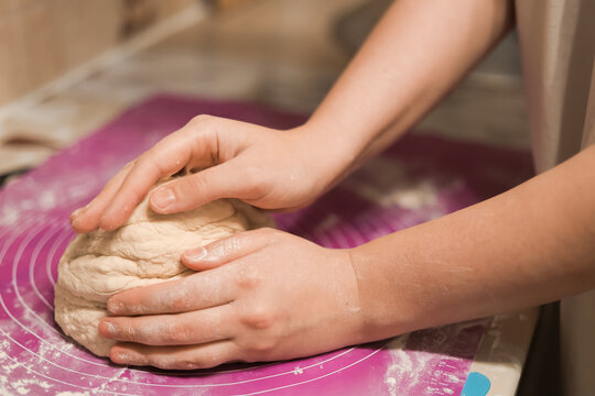 A close-up shot of hands firmly kneading a fresh ball of light-colored dough on a pink or purple silicone baking mat.