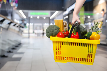 Customer holding shopping basket with different food products at supermarket, closeup