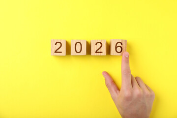 New 2026 year. Man putting cube with number 6 on yellow background, top view