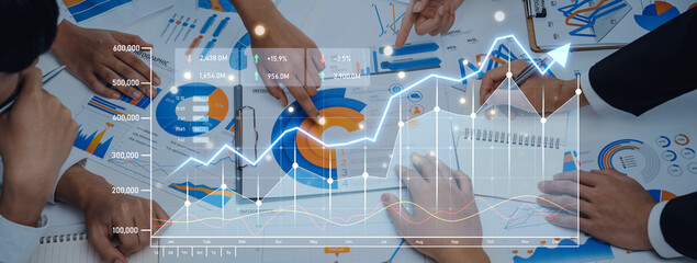 A business team collaborates during a meeting, analyzing financial graphs and charts with digital overlays. Demonstrates teamwork and strategic planning in an office environment. Scalp