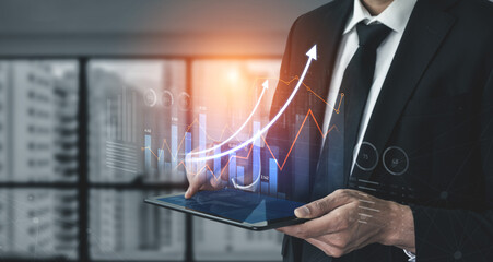 A businessman in a suit uses a tablet to analyze financial data with emerging graphs and charts in a modern office, reflecting trends of growth and success in the background. Scalp