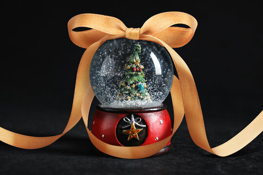 Snow globe with Christmas tree inside and golden bow on black background
