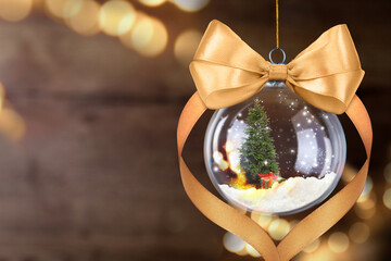 Christmas ball with golden bow against blurred lights on dark background. Beautiful festive ornament
