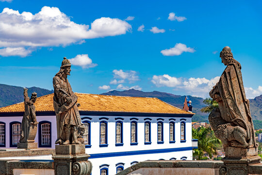 Statues of biblical prophets sculpted by Aleijadinho with ancient buildings and mountains in the background in Congonhas, Minas Gerais.