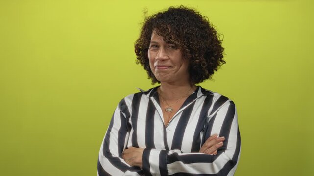 Middle aged hispanic woman crosses arms in studio with striped shirt and necklace on green backdrop; denial.