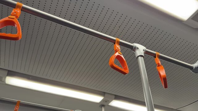 Ceiling mounted handrail with bright colored triangular hanging grips for public transportation. Dangling handgrips for maintaining balance on buses and subway cars while transportation is in motion
