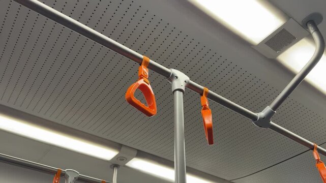 Plastic hanging handrail for standing passengers in train car dangles while moving in light colored interior. Concept for balance and safety while traveling on public transportation