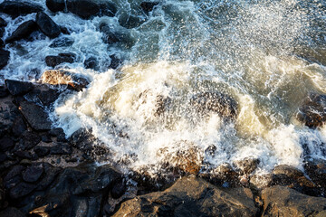 Obraz premium Ocean waves crashing against the beach rocks, light reflecting on the water.
