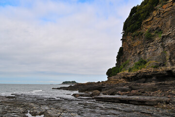 A strange rock cliff next to the sea under the blue sky