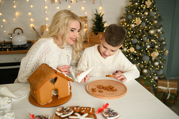 A mother and son are preparing a gingerbread house for the Christmas and New Year holidays.
