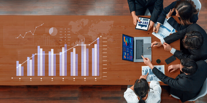 A diverse team of professionals engages in a business meeting, analyzing graphs and data trends on electronic devices to drive informed decision-making. Scalp