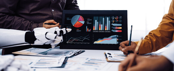 A business team engages with robotic technology while analyzing various data visualizations and charts, focusing on strategic decision-making in the modern workplace.Noogenesis