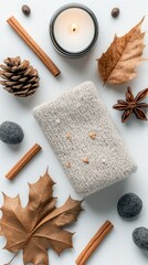A collection of autumn-themed objects arranged on a white surface, including a lit candle, a knitted item, and natural elements.