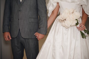 Couple holding hands in elegant wedding attire with a beautiful bouquet during a romantic ceremony...