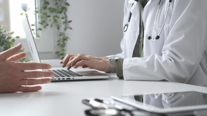 Doctor wearing lab coat and stethoscope typing on laptop keyboard and explaining something to patient during a medical consultation in hospital office. Medicine and health care concept - Powered by Adobe