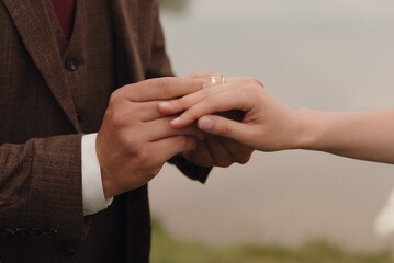 Couple exchanges wedding rings by a serene lake during their intimate outdoor ceremony