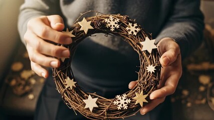 Woman holding a handmade Christmas wreath with stars and snowflakes for holiday seasonal decoration.