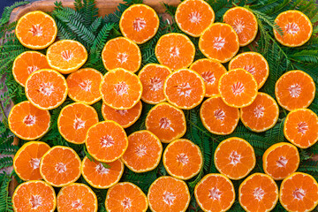 Sliced oranges arranged on a wooden surface with green leaves. The vibrant orange color contrasts with the natural greenery, creating a fresh and appetizing scene.