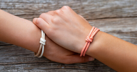 Close-up of two hands holding each other wearing matching knotted rope bracelets symbolizing friendship and connection on wooden background