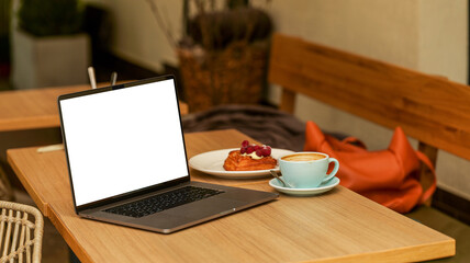 Laptop with blank screen, coffee, and pastry on a cafe table