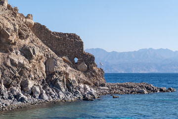 Ancient Stone Ruins Alongside a Serene Coastline With Clear Blue Waters and Distant Mountains in the Background on a Sunny Day