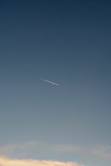 A jet stream flies across a gradient blue sky on a partly cloudy day.