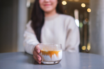 Closeup image of a woman holding and serving a glass of dirty coffee