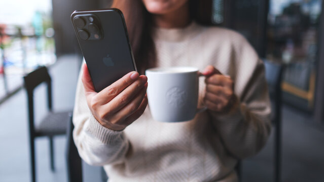 Nov 10th 2025 : A woman holding and using Iphone 15 Pro Max smart phone while drinking coffee in Starbucks coffee shop, Chiang mai Thailand