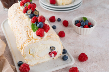 Meringue Pavlova roll cake with cream and fresh berries on top on a ceramic board on a concrete background. Copy space.